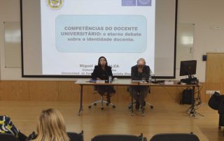 Duas pessoas sentadas no palco a fazer uma apresentação num auditório