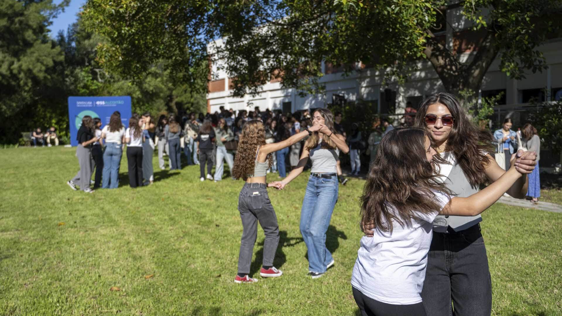 Duas mulheres a dançar com um grande volume de pessoas na relva, no Open Day da ESAALCOITÃO