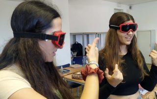 Duas alunas com óculos colocados a experienciar como ser invisual