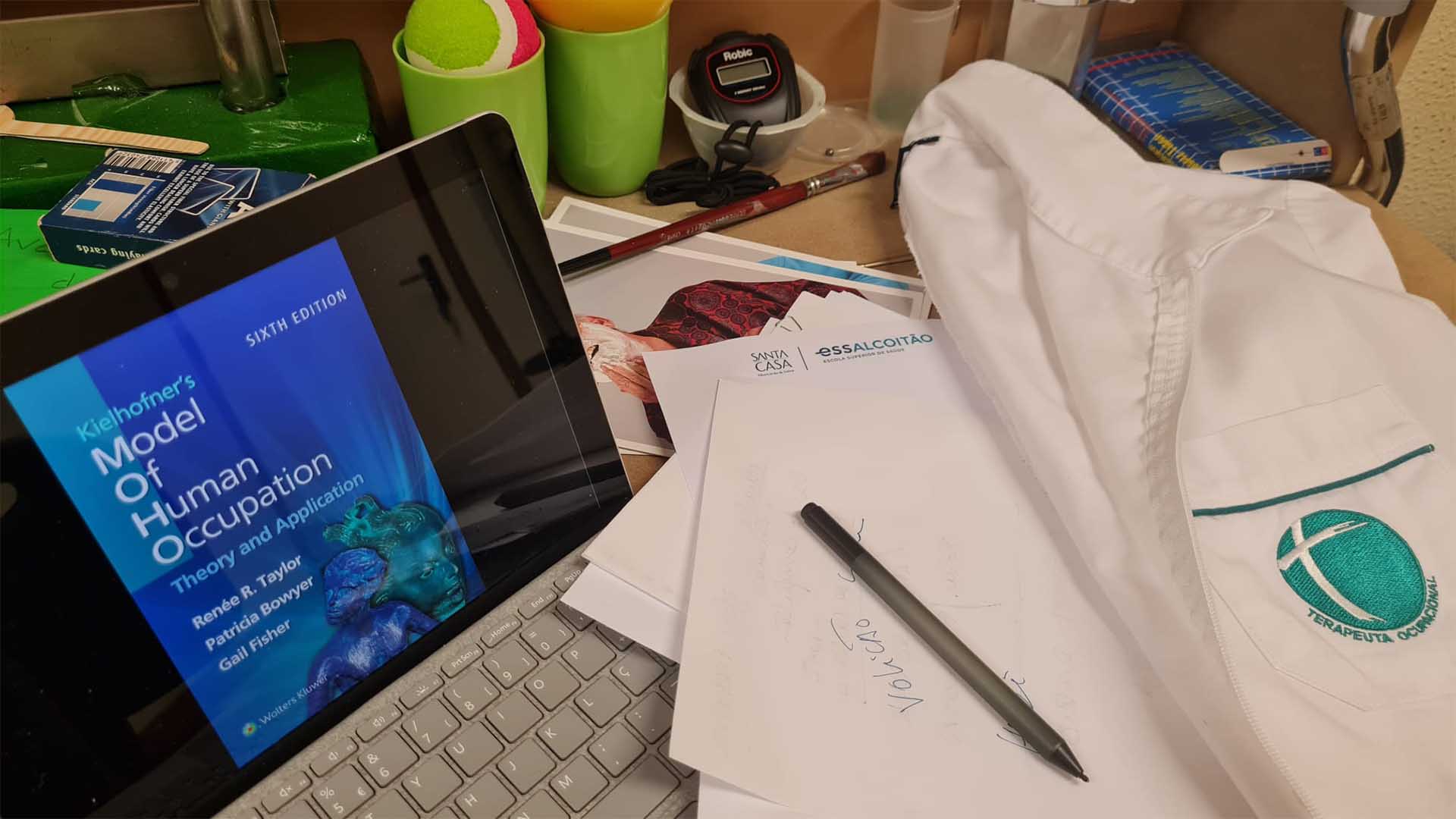 computador aberto e uma bata da Terapia Ocupacional pousada na mesa