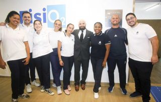 Grupo de alunos da ESSALCOITÃO com o Professor Vítor Hugo Azevedo, posa para a fotografia durante a inauguração da Unidade de Fisioterapia Cardiorrespiratória e Sarcopenia (FisiO2). Estão num espaço interior, junto a uma parede com o logótipo “FisiO2”, e todos sorriem para a câmara.