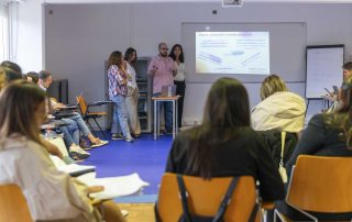 Grupo de alunos da Pós-Graduação em ITEPDDM em roda sentados e atentos ao que um dos grupos está a apresentar no projetor