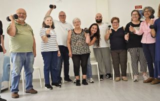 Fotografia de um grupo de idosos muito sorridentes com halteres na mão, juntamente com fisioterapeutas