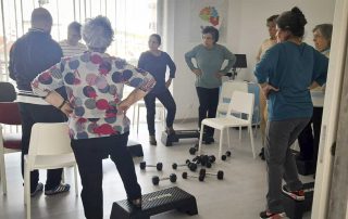 Grupo de idosos a fazer exercícios de fisioterapia com aconselhamento. No caso, estão com o pé em cima de uma box