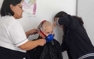 Duas fisioterapeutas a colocar uma máscara respiratória a uma senhora idosa
